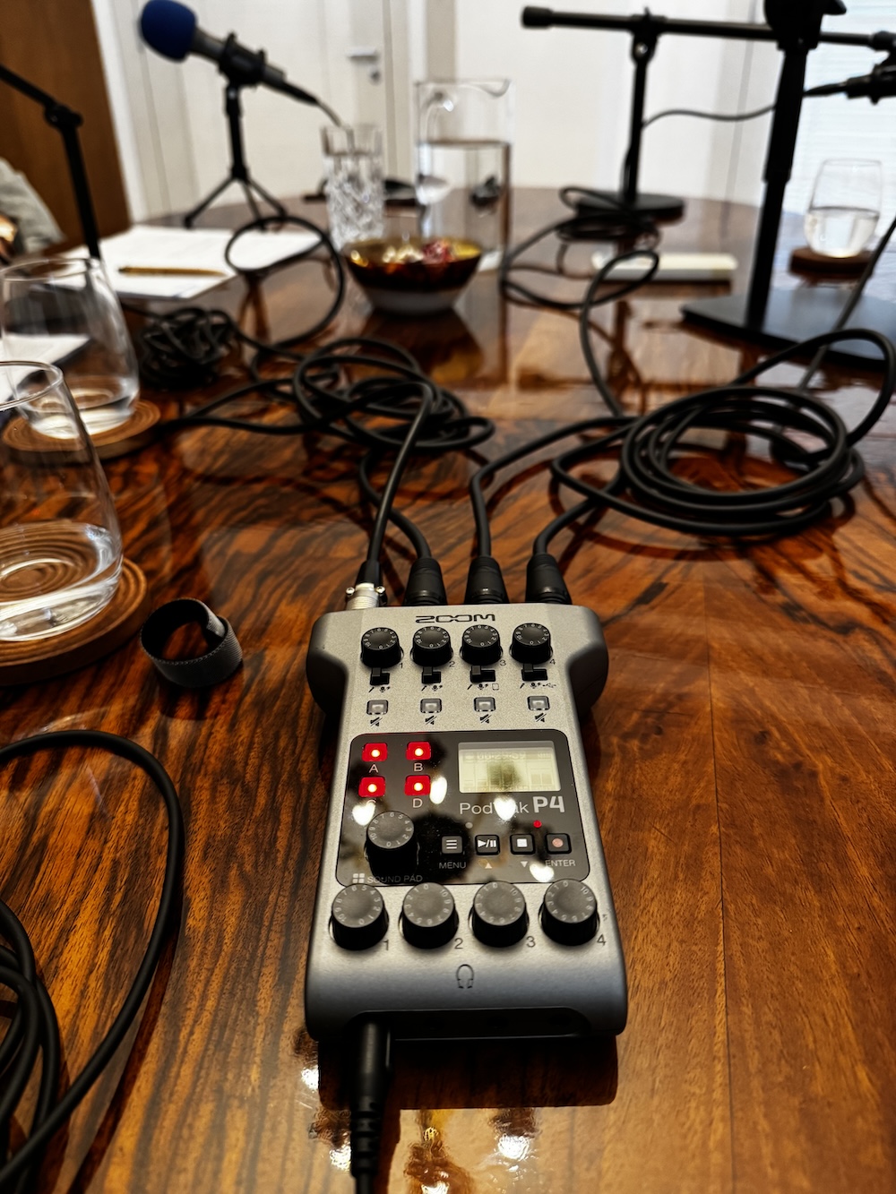 Mobilne studio na stole: rejestrator Zoom PodTrak P4, mikrofony na statywach i szklanki z wodą przed nagraniem